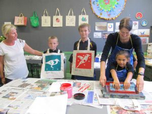 Waitotara Principal Jane Corcoran with pupils Bruce Butters-Fitton and Cooper Mackintosh displaying their completed tote bags while Sarjeant educator Sietske Jansma assists Kimberley Frewin with the screen printing process.